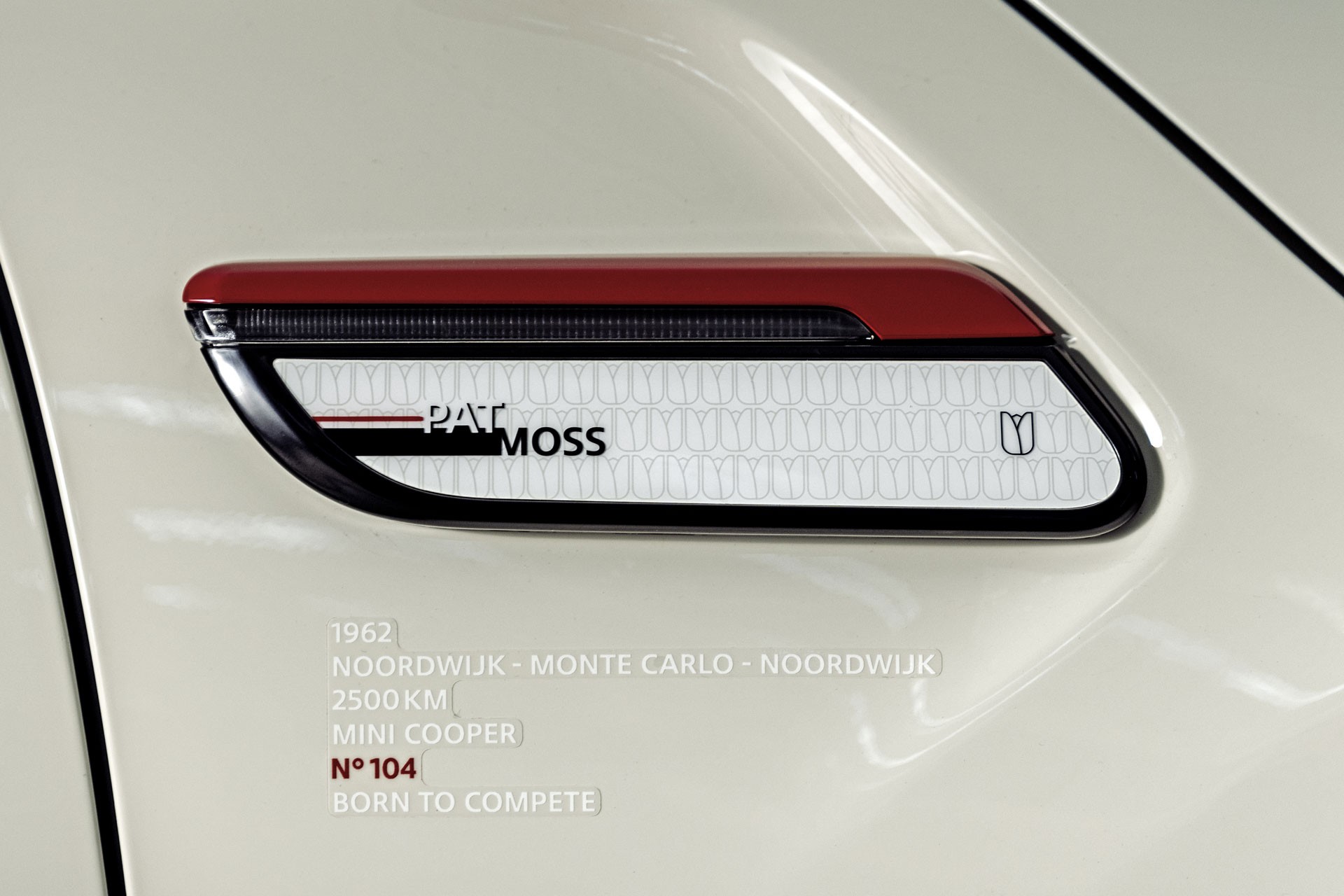 Close-up of the side scuttles with a Pat Moss labeling on the Pepper White John Cooper Works model. Below it you will find the following facts: “Year: 1962, Racing Route: Noordwijk- Monte Carlo- Noordwijk, Racing Length: 2500 km, Vehicle: MINI Cooper, Starting number: 104, Born to compete.”